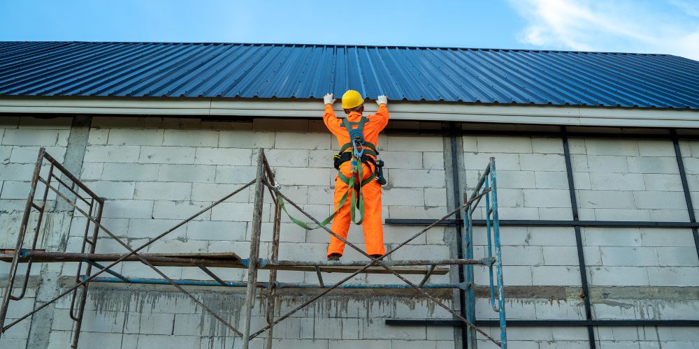 A man in a hard hat, safety suit, and harness inspecting a roof.