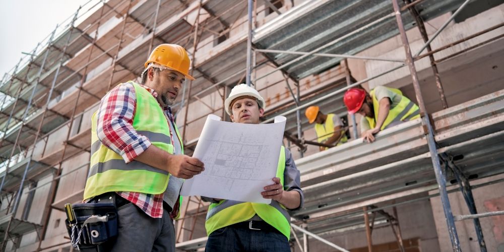 Men with hard hats holding a blueprint, planning for the roof.
