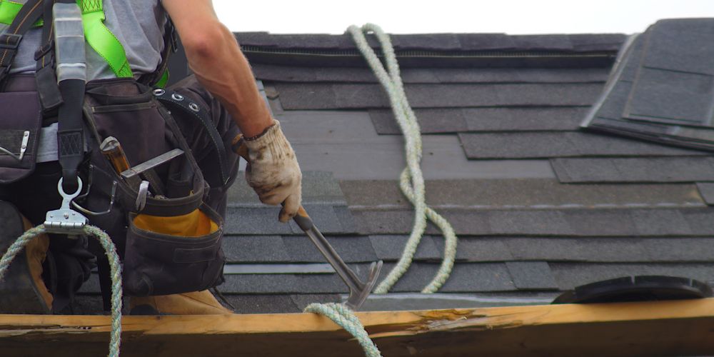 A man on roof holding a hammer with safety harness